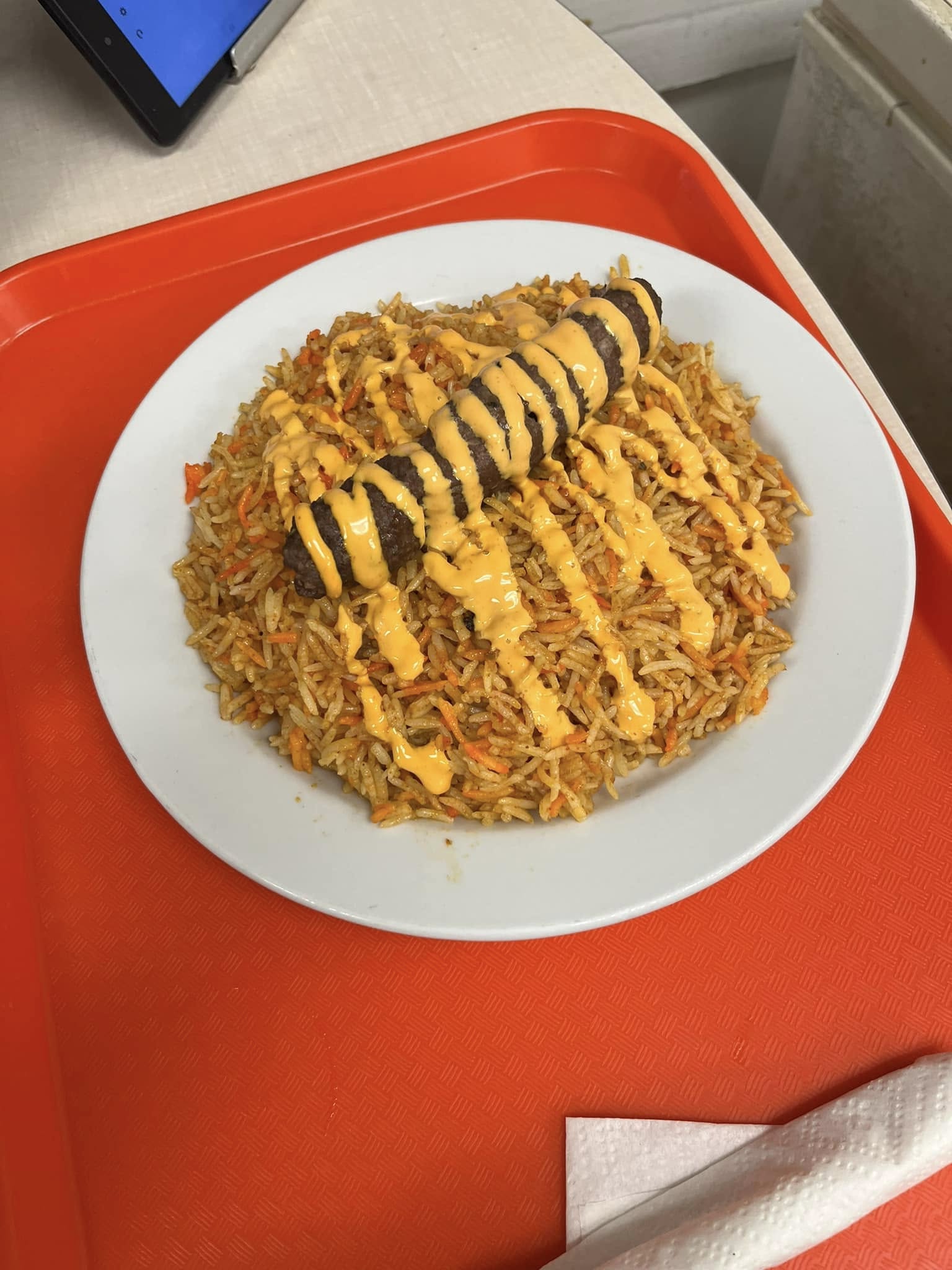 Seekh kababs over spiced rice with a sauce drizzle on a white plate
