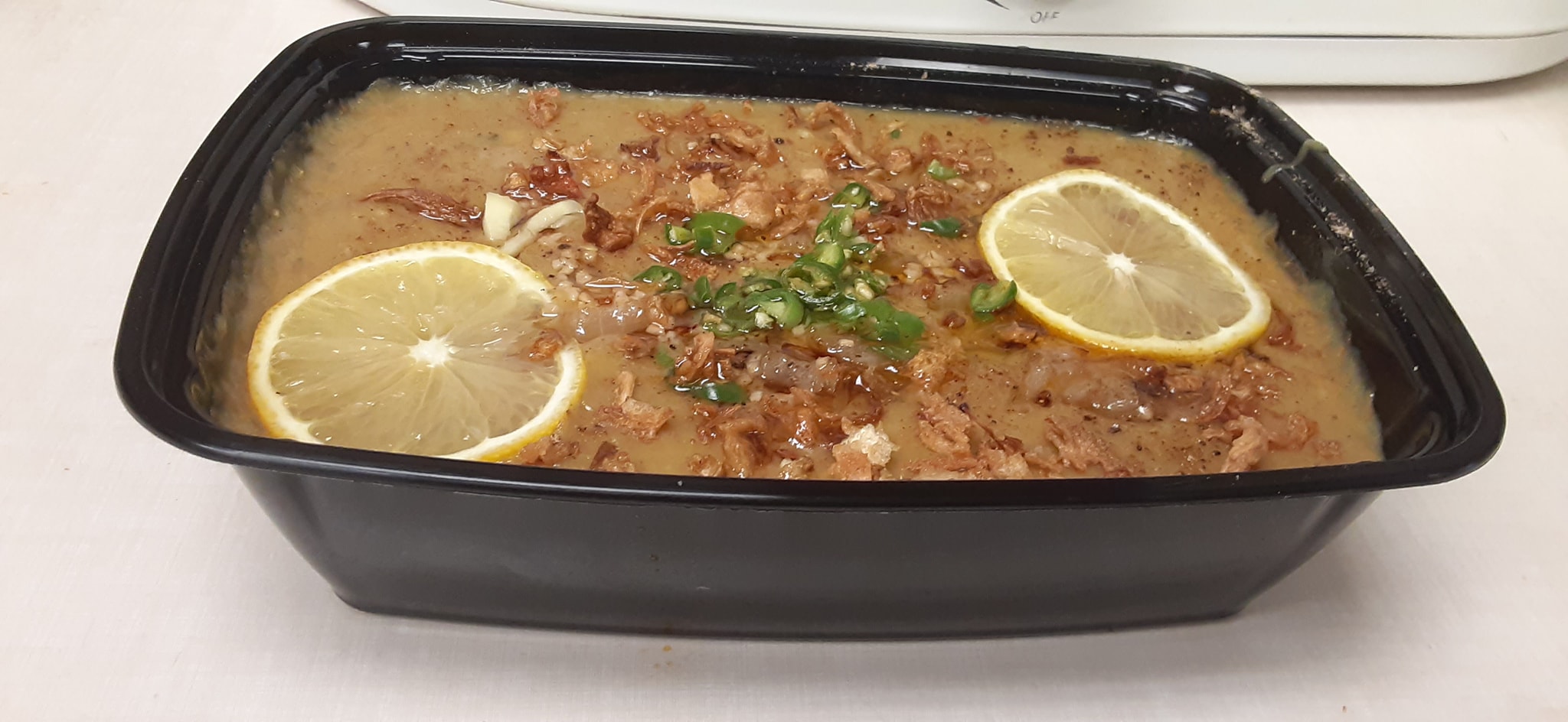 Slow-cooked beef curry in a takeout container with fried onions, green chili and lemon