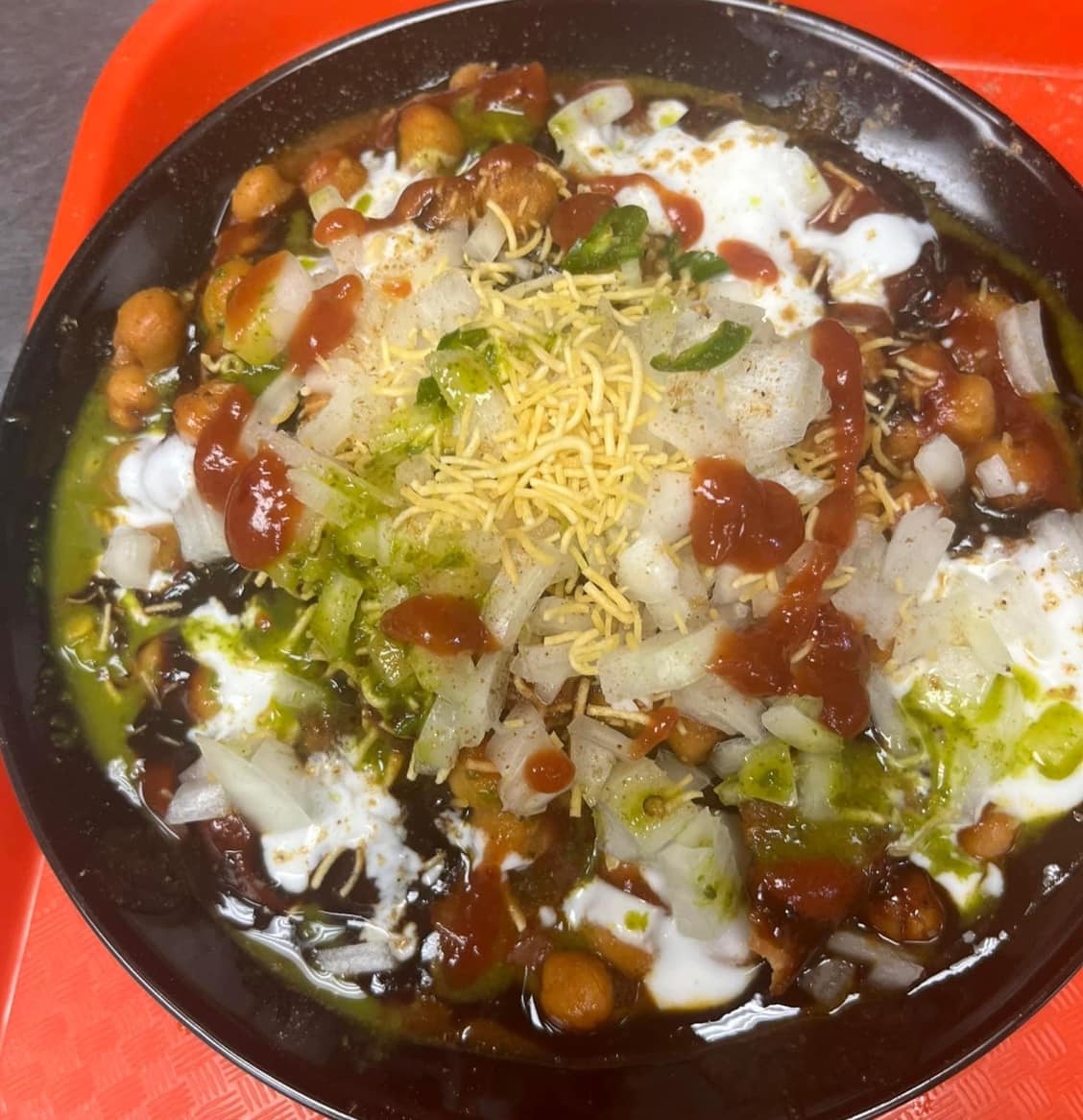 Chana chaat in a black bowl with yogurt, chutneys, onions and sev